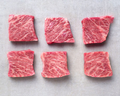 Six square-cut marbled wagyu pieces in two rows on a pale grey surface