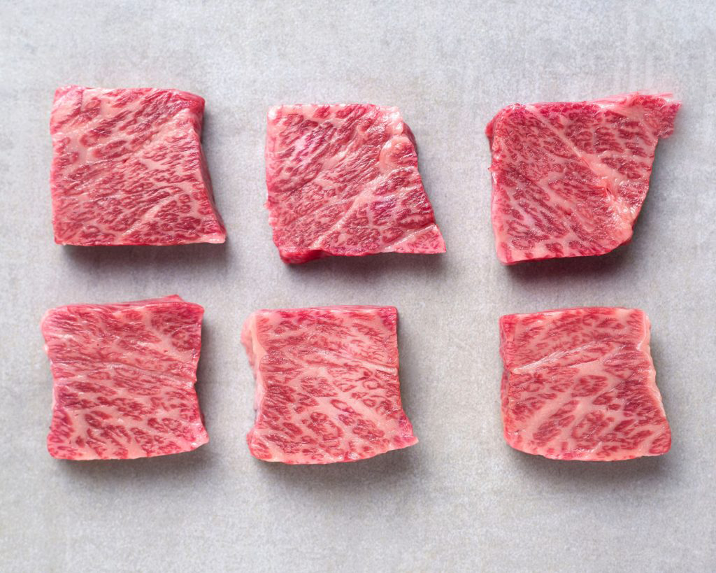 Six square-cut marbled wagyu pieces in two rows on a pale grey surface