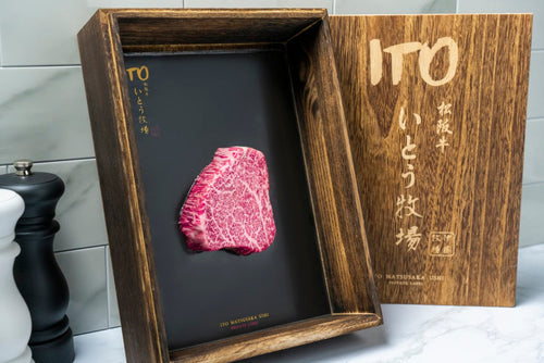 Raw marbled steak in an open wooden box with Ito lettering on its lid