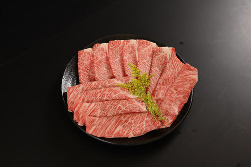 Thin marbled wagyu slices fanned on a round black plate with a flowering sprig