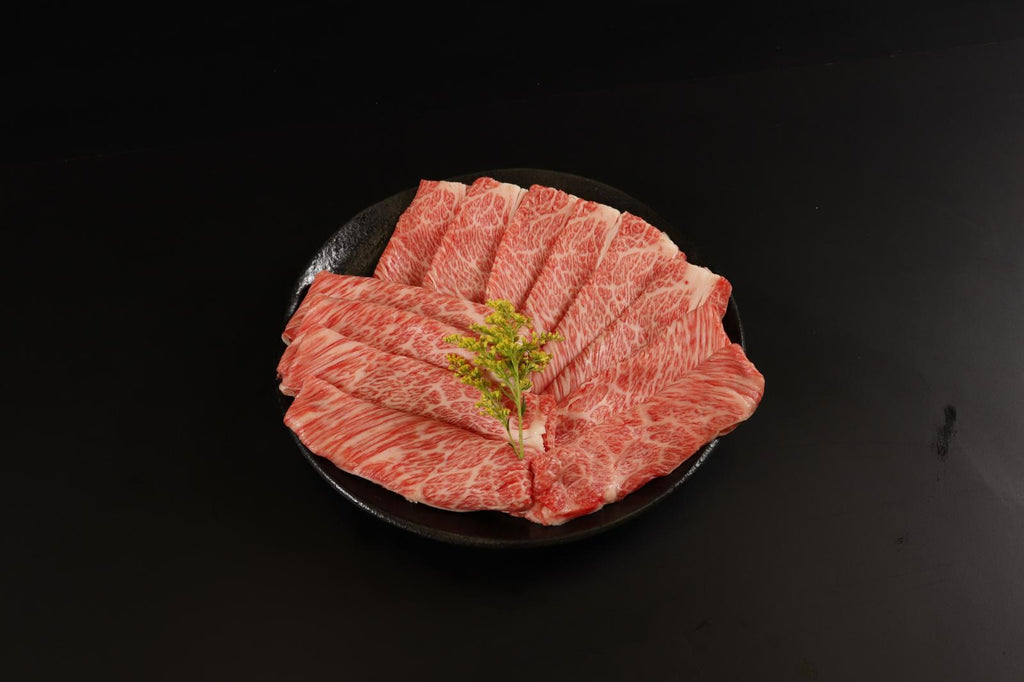 Wider view of fanned marbled wagyu slices on a black plate on a dark surface