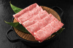 Folded marbled wagyu slices on a wooden board in a black dish with green leaves
