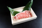 Raw marbled wagyu steak in a pale wooden tray with two green leaves