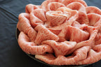 Thin marbled wagyu slices ruffled into a rose-like mound on a dark plate