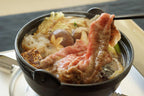 Chopsticks lifting a cooked slice from an iron pot with tofu, mushrooms and noodles