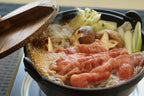 Wooden lid lifted from an iron pot of wagyu simmering with mushrooms, leeks and noodles