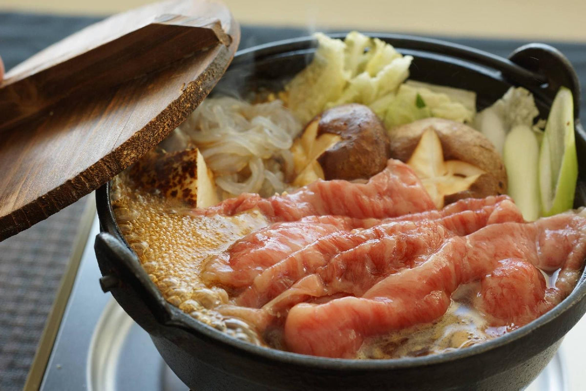Wooden lid lifted from an iron pot of wagyu simmering with mushrooms, leeks and noodles